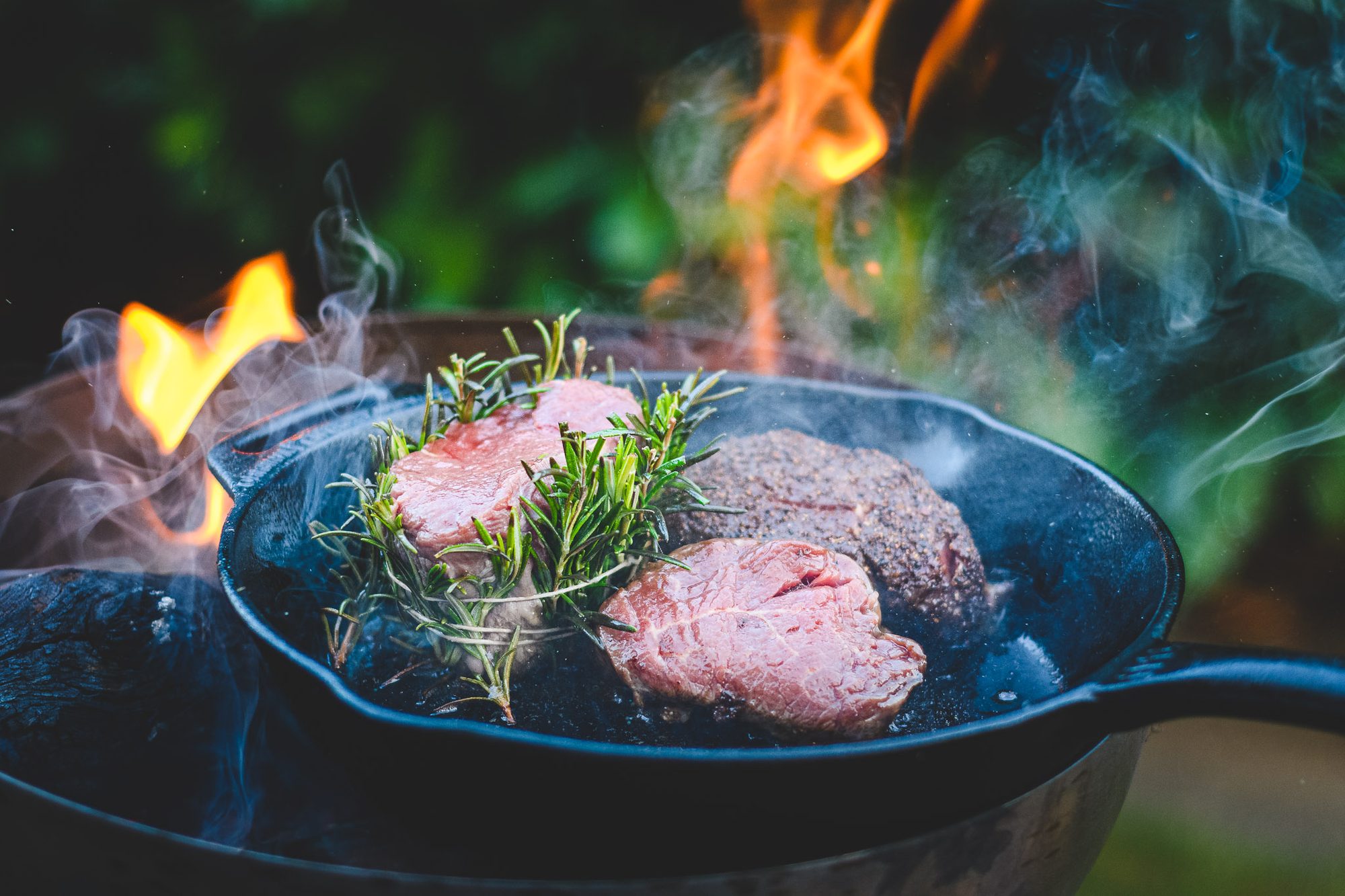 Steaks mit Rosmarin in einer gusseisernen Pfanne über offenem Feuer